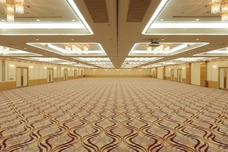 テーブルや椅子が配置されていない、遮るもののない圧倒的な広さを持つ大宴会場の全景。床一面には波打つような幾何学模様の絨毯が広がり、開放感あふれる空間です。