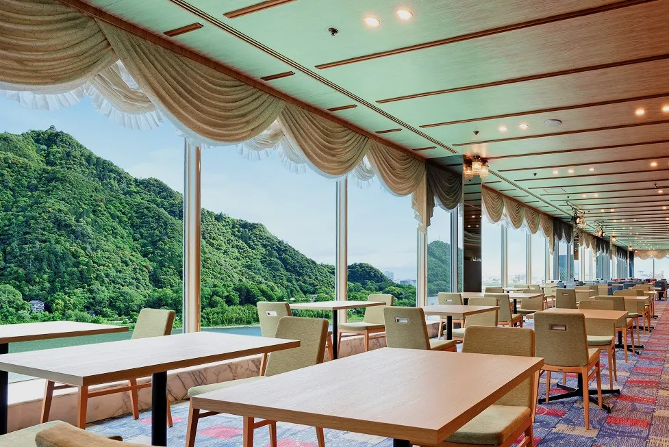 大きな窓から一面に広がる緑豊かな山の景色を眺めながら、ゆったりと食事が楽しめる、開放的で落ち着いた雰囲気のレストラン内観。