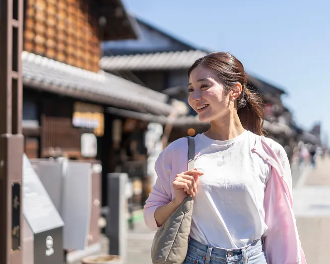 歴史的な和風の街並みをバックに、笑顔で歩く旅行中の女性。