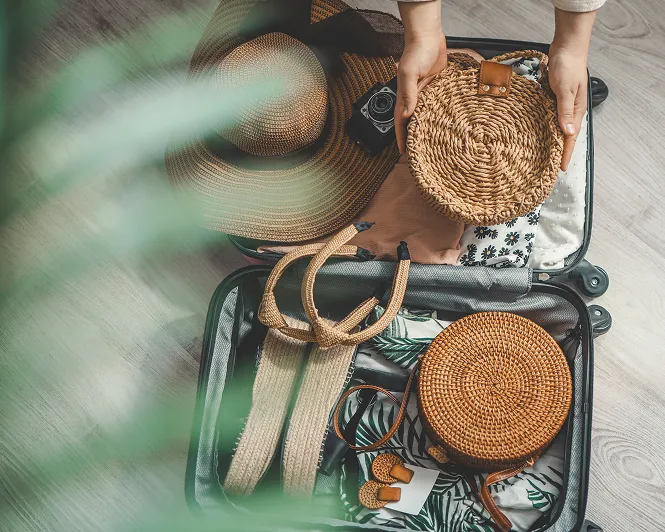 開いたスーツケースに帽子やバッグなどの旅支度をパッキングする様子。