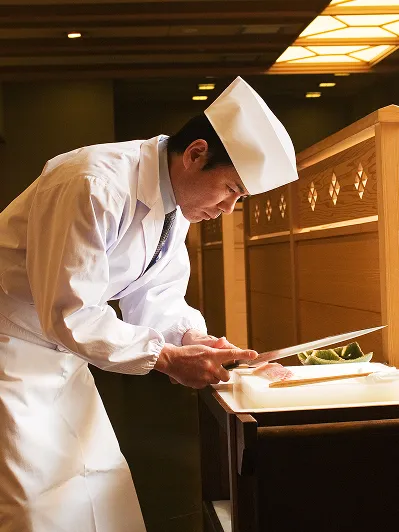 高級感のある和の空間で、包丁を手に真摯な眼差しで調理に臨む和食の職人。