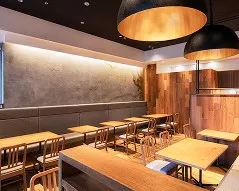 木目調のテーブル席とベンチシートが並ぶ、温かい照明のモダンなレストラン内装。