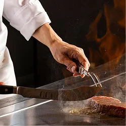 シェフが目の前の鉄板で炎と湯気を上げながら手際よくステーキを焼き上げるライブ感あふれる調理風景。
