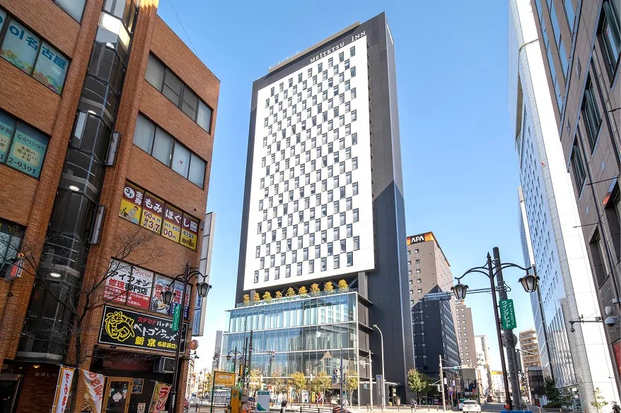 青空のもと、都会の街並みにスマートにそびえ立つ名鉄インの高層ビル外観。