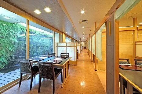 日本料理 吉祥・炉端コーナーの内観。大きな窓から緑の壁面が見える、和モダンで落ち着いた雰囲気のテーブル席。
