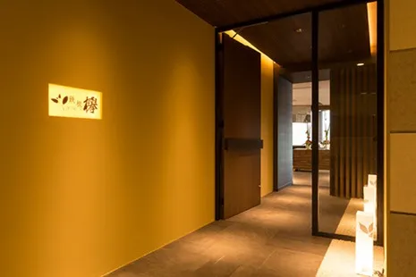 鉄板「欅」の外観。温かみのある黄色い壁にロゴ看板が光る、モダンでスタイリッシュな入り口。